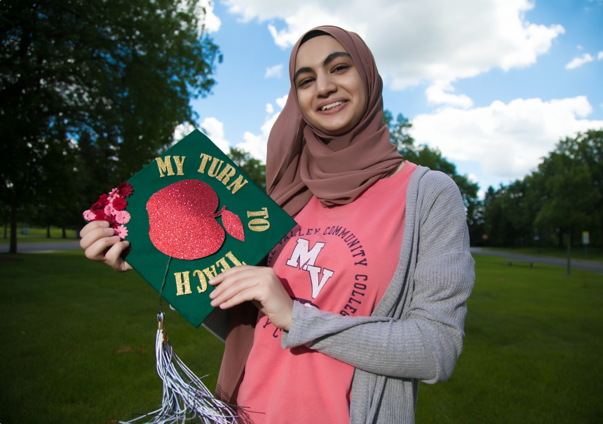 Rama Diab, current student at GSU, holding a graduation cap that says, ‘my turn to teach’