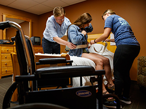 OT professor and student practice assisting a patient moving from a bed to a wheelchair with another student OT professor and student practice assisting a patient moving from a bed to a wheelchair with another student