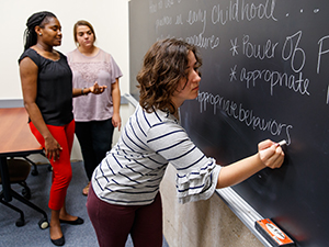 Student writing on chalkboard while other students watch