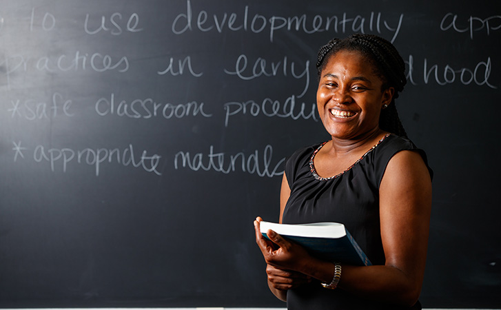 Student holding book in front of chalkboard