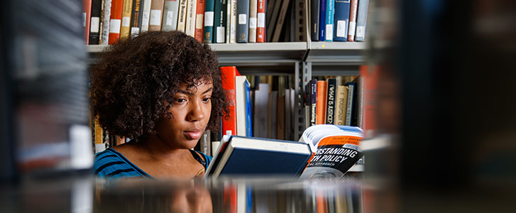 Student reading book near bookshelf in the university library