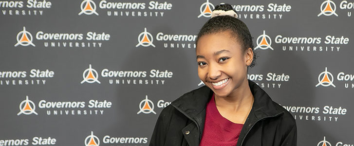 Student smiling while standing in front of back drop with a repeated Governors State logo