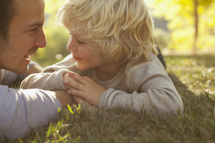 Parent and child laying on grass smiling at each other