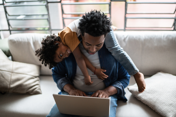 Parent typing on laptop while child is laying across their shoulders